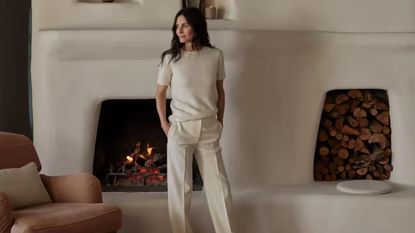 Courtney Cox in white outfit posing in front of fireplace