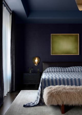 color drenched blue bedroom with matching bedding, green artwork and fluffy ottoman