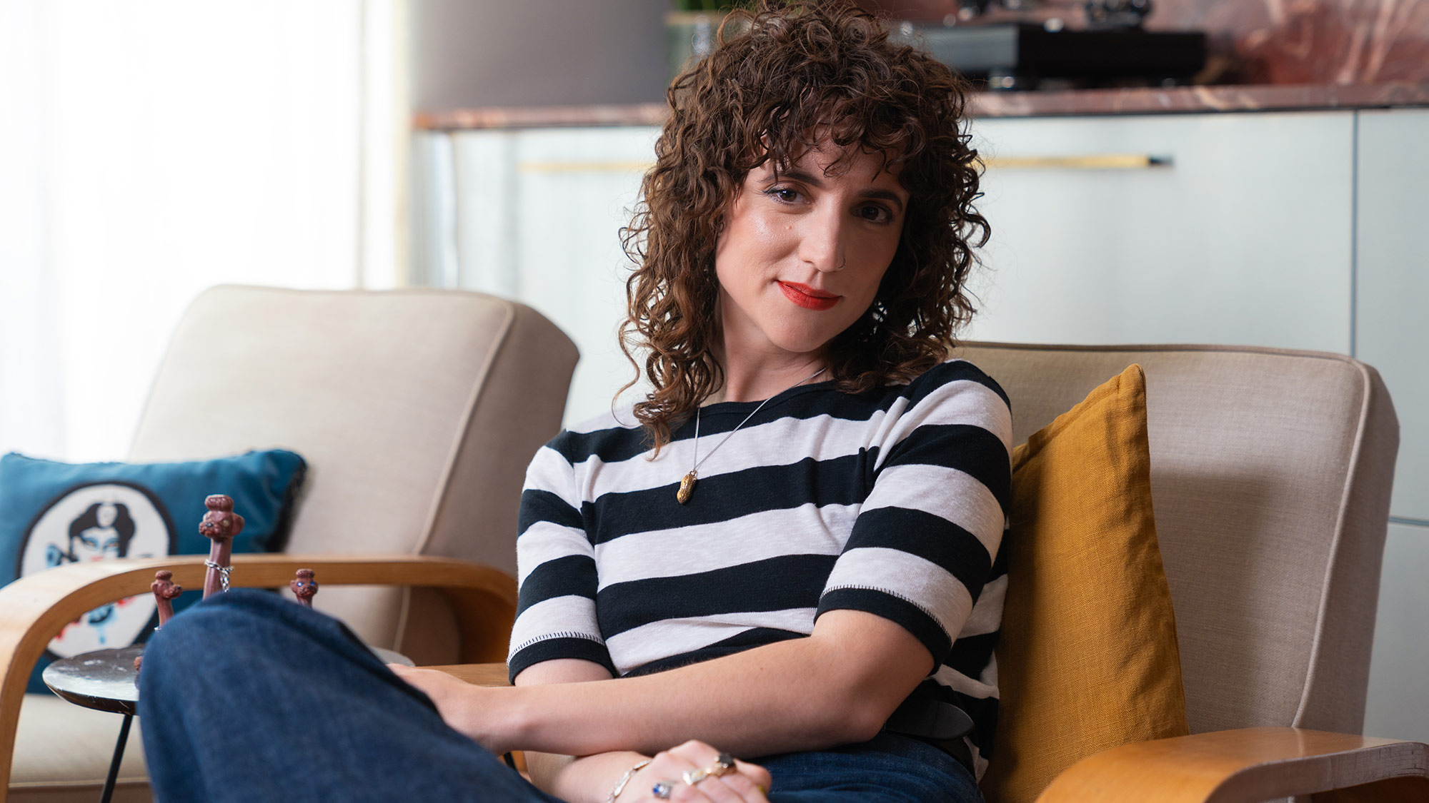 Pippa Toole poses for a portrait and wears a striped top whilst sitting on a sofa