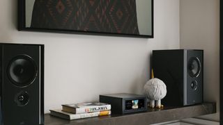 NAD M10 V3 on a wooden shelf with speakers and books