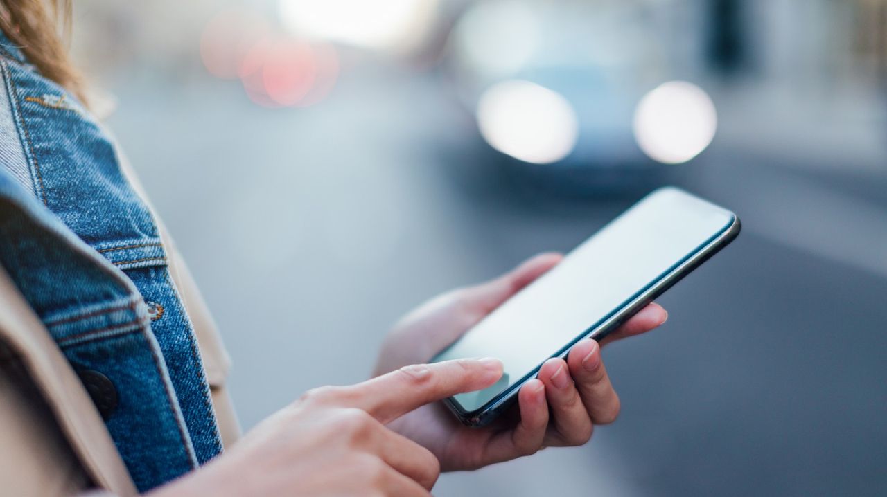 Close-up shot of female hands using smartphone in the city while waiting for transport.