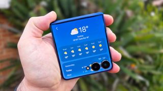 In-hand image of the Samsung Galaxy Z Flip 7 with garden in the background