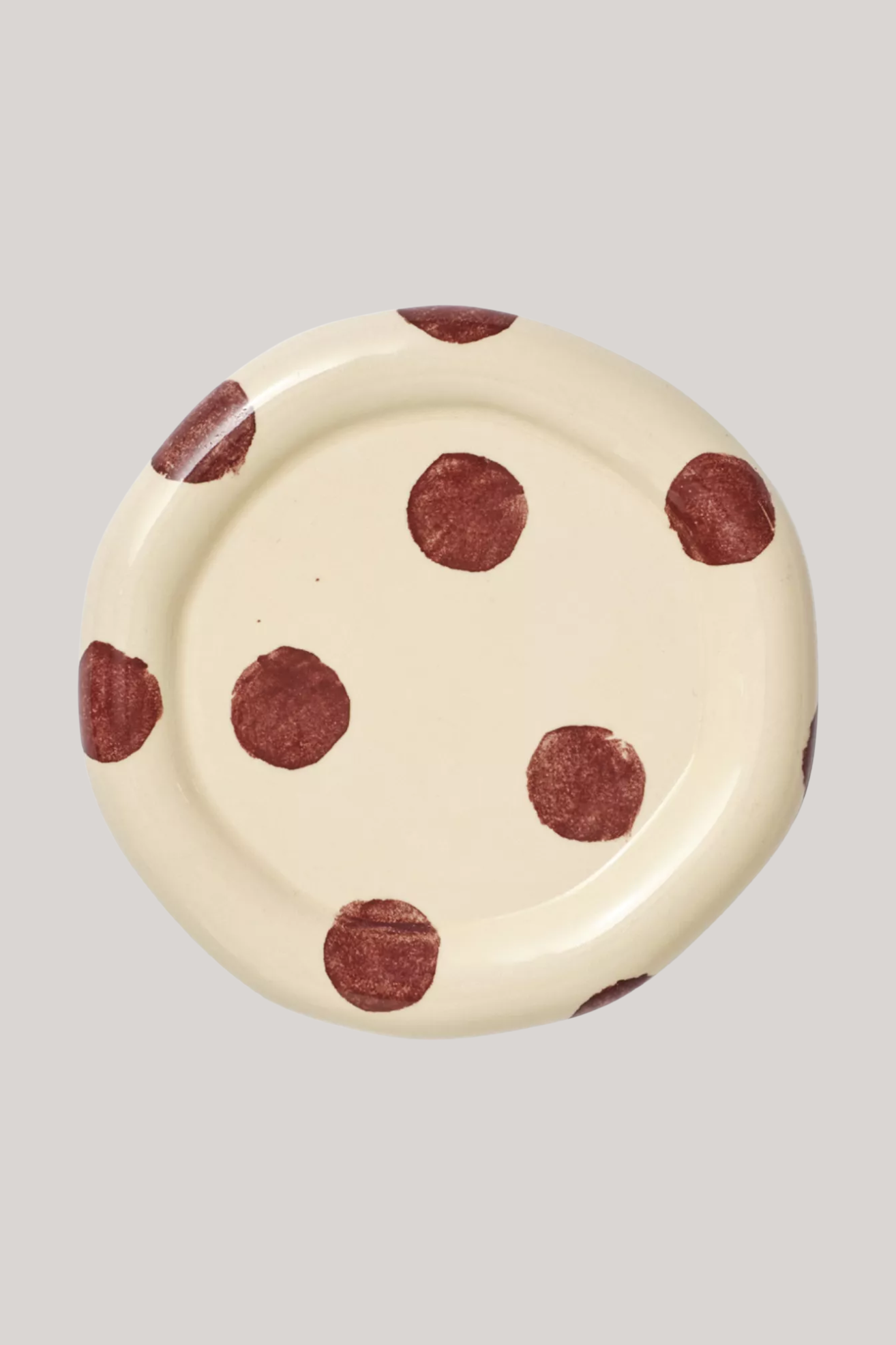 A chubby ceramic saucer in butter yellow with burgundy polka dots
