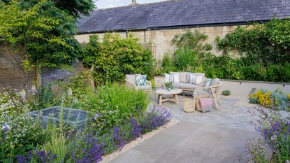 A garden with a paved patio, flower borders, and a garden furniture set