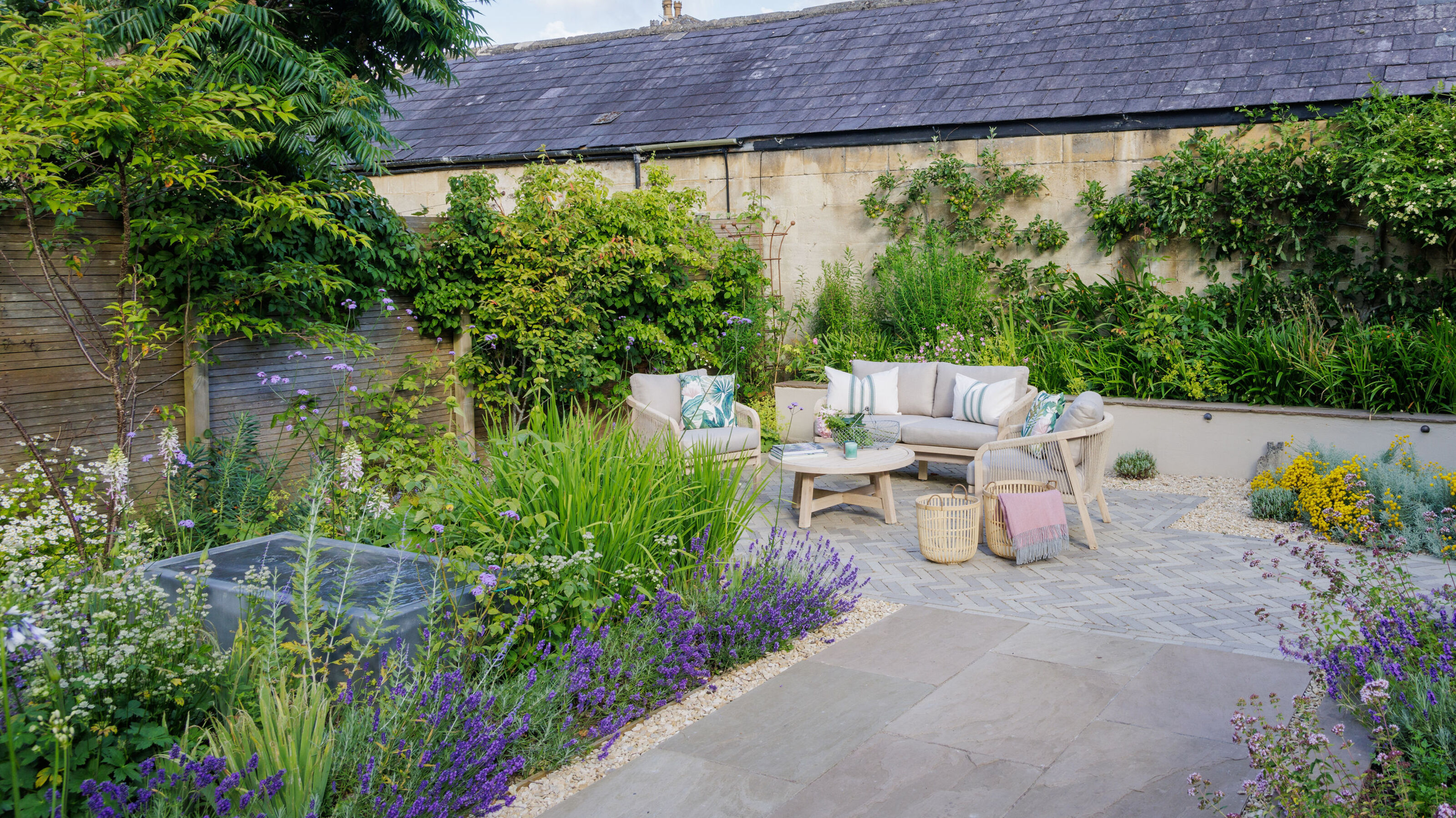 A garden with a paved patio, flower borders, and a garden furniture set