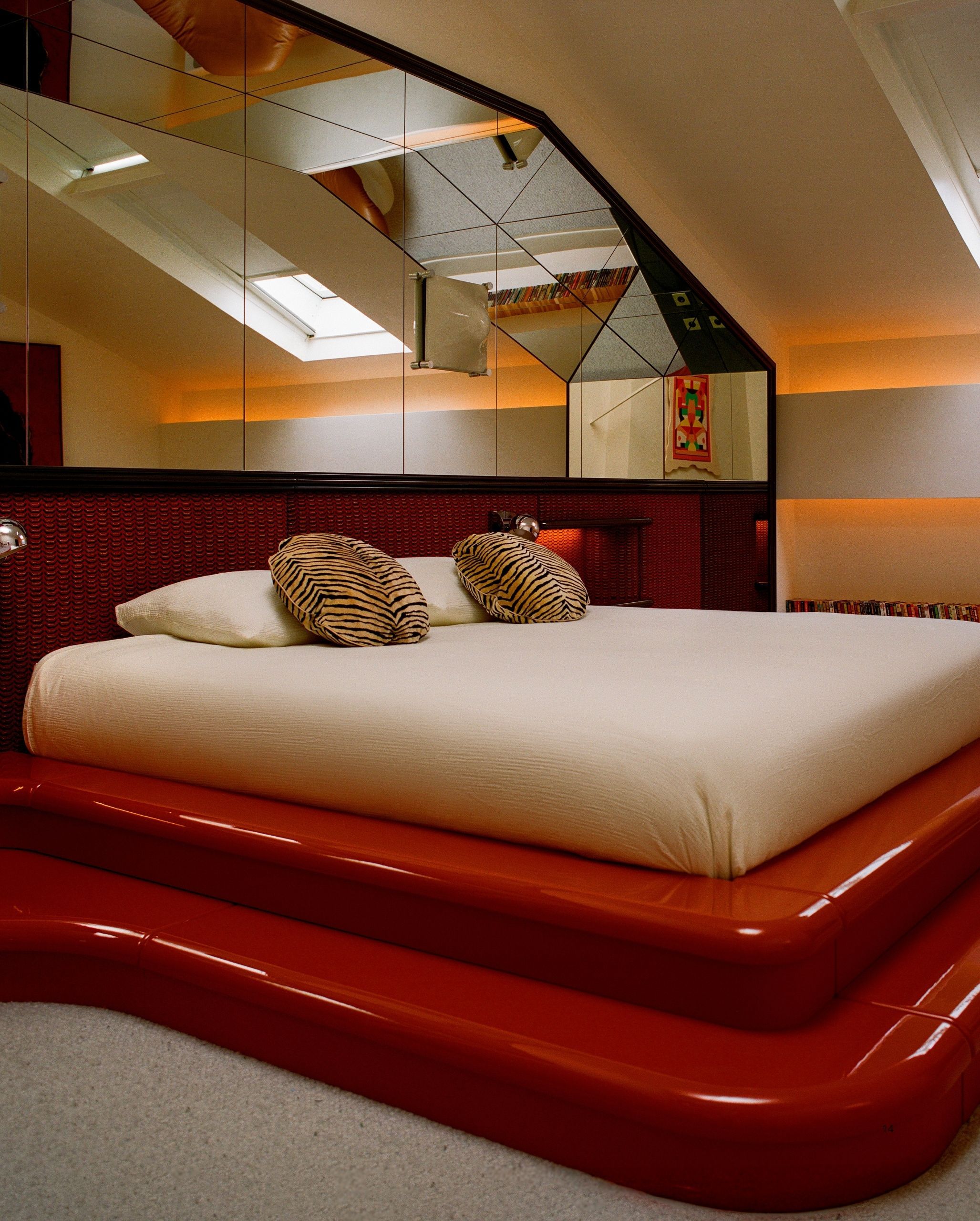 A bedroom with a built-in bed that has red lacquer steps up to it that wrap around the wall. The wall is a red fabric with mirror on the upper half. There is a zebra pillow on the bed.