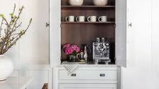 home coffee bar in cabinetry, with coffee machine, vase of flower, jug, tea towel, and coffee cups