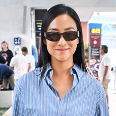 Greta Lee wearing a striped button-down shirt, blue jeans, and black boots