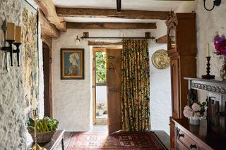 whitewashed hallway with beams and flagstone with door open and tapestry and grandfather clock and dark wood furniture