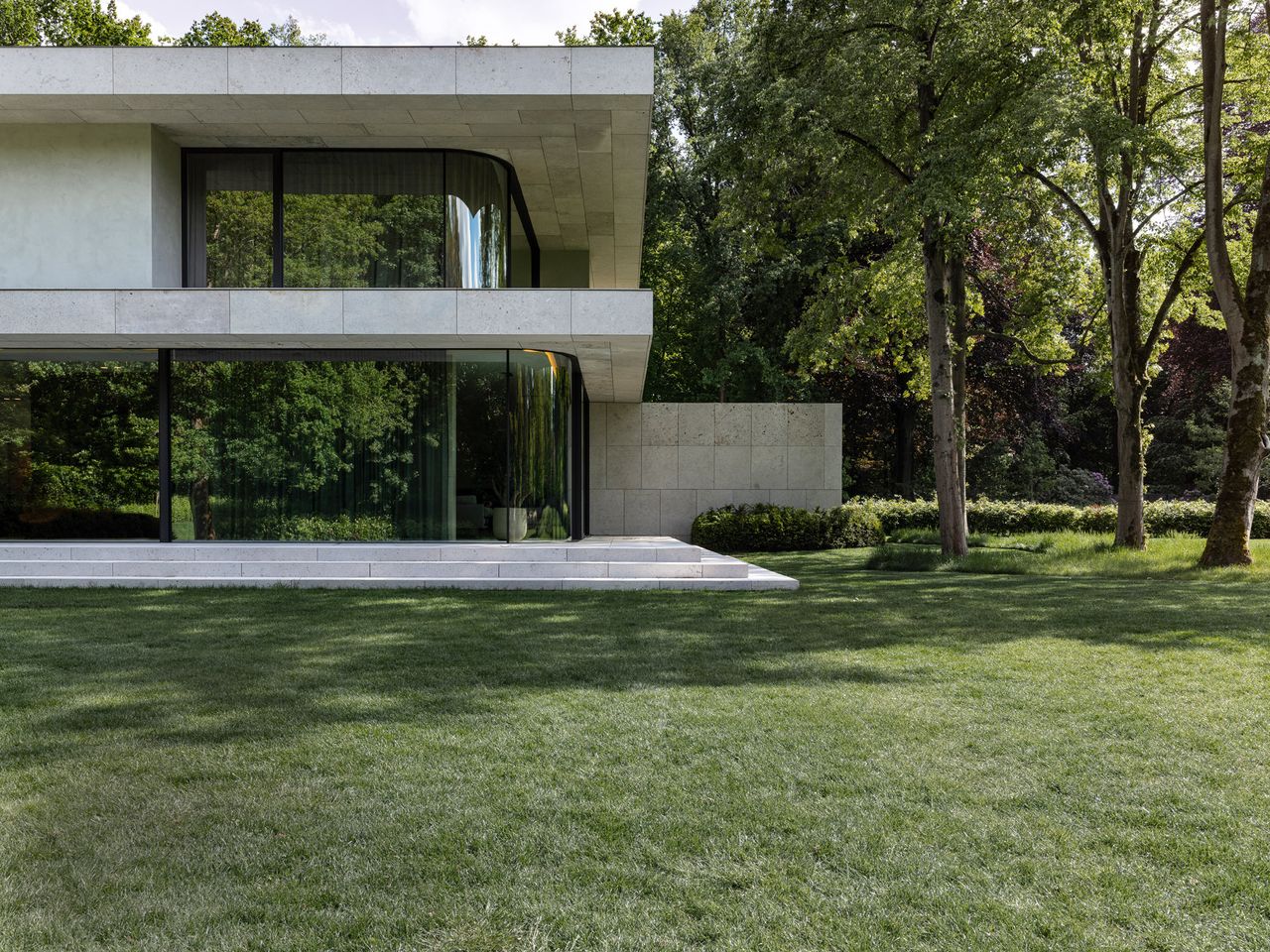 Shimmering glass villa with greenery and trees surrounding it