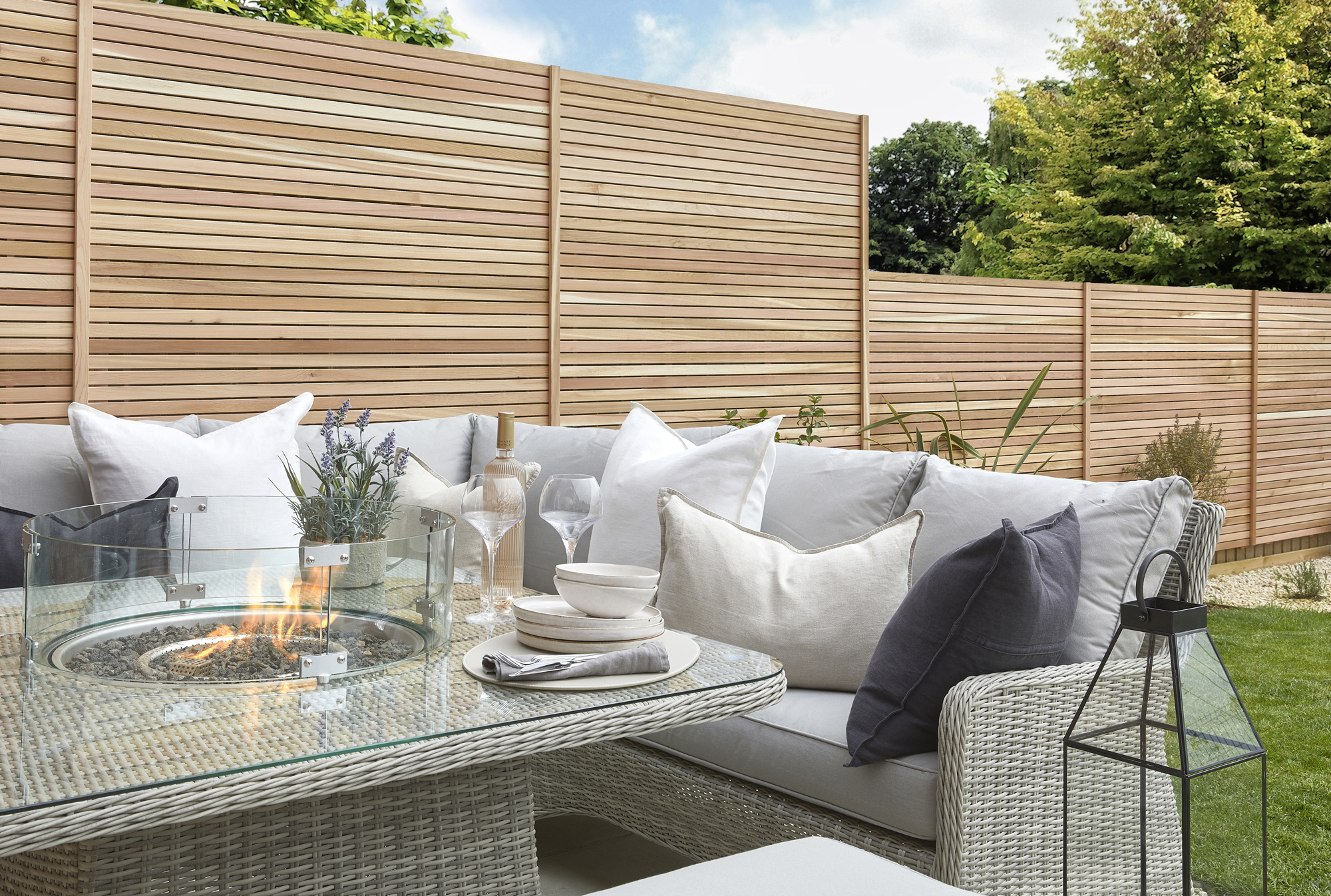 A garden with an rattan outdoor furniture set and tall slat fencing