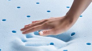 A person presses their hand into a blue-colour Gel Foam Mattress Topper and it leaves an indent