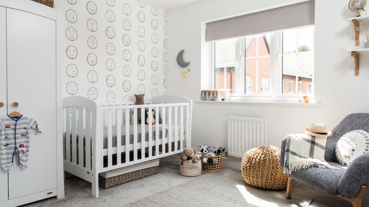 Grey walls, white cot with bars, grey carpet, white wardrobe and cuddle toys and footstool