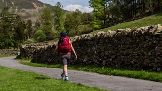 A woman walks along a country lane wearing a red Gregory Jade LT 24 backpack.