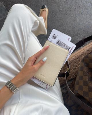 Woman traveling, holding passport case with boarding pass and white jeans with ballet flats.