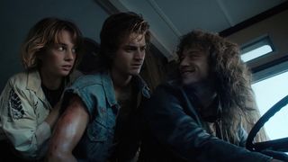 Eddie sits at the wheel of a bus while Robin and Steve watch on in Stranger Things season 4