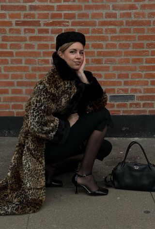 winter tight outfit shown in a photo of a woman wearing a black hat, leopard print coat, black sweater, black capri pants, black sheer tights, black ankle strap pumps, and a black handbag