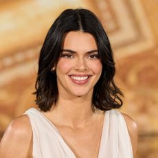 Kendall Jenner walks the runway wearing a white dress in front of a gold background