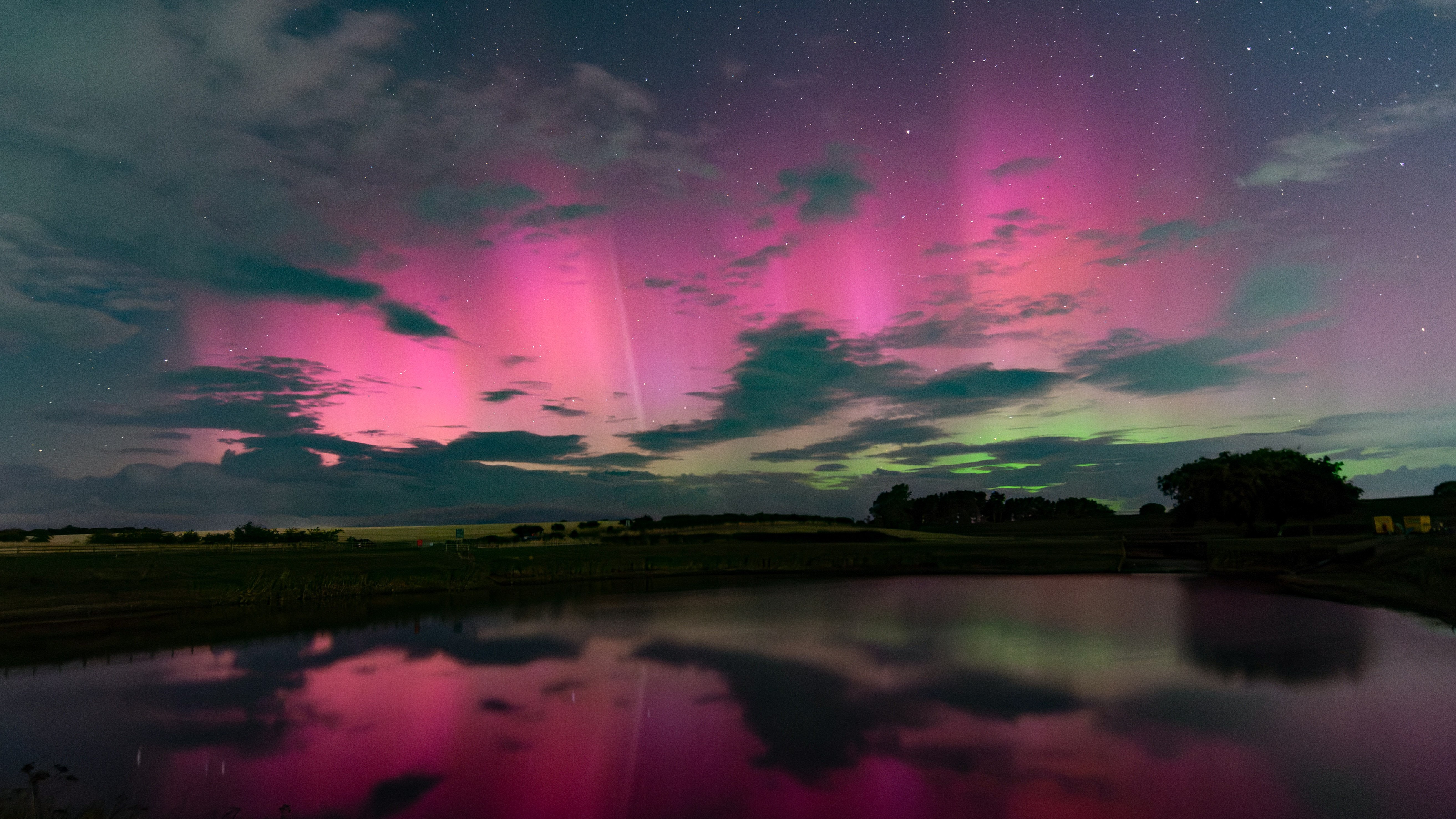 northern lights appear as ribbons of pink and green light above a body of water, they are reflected below.