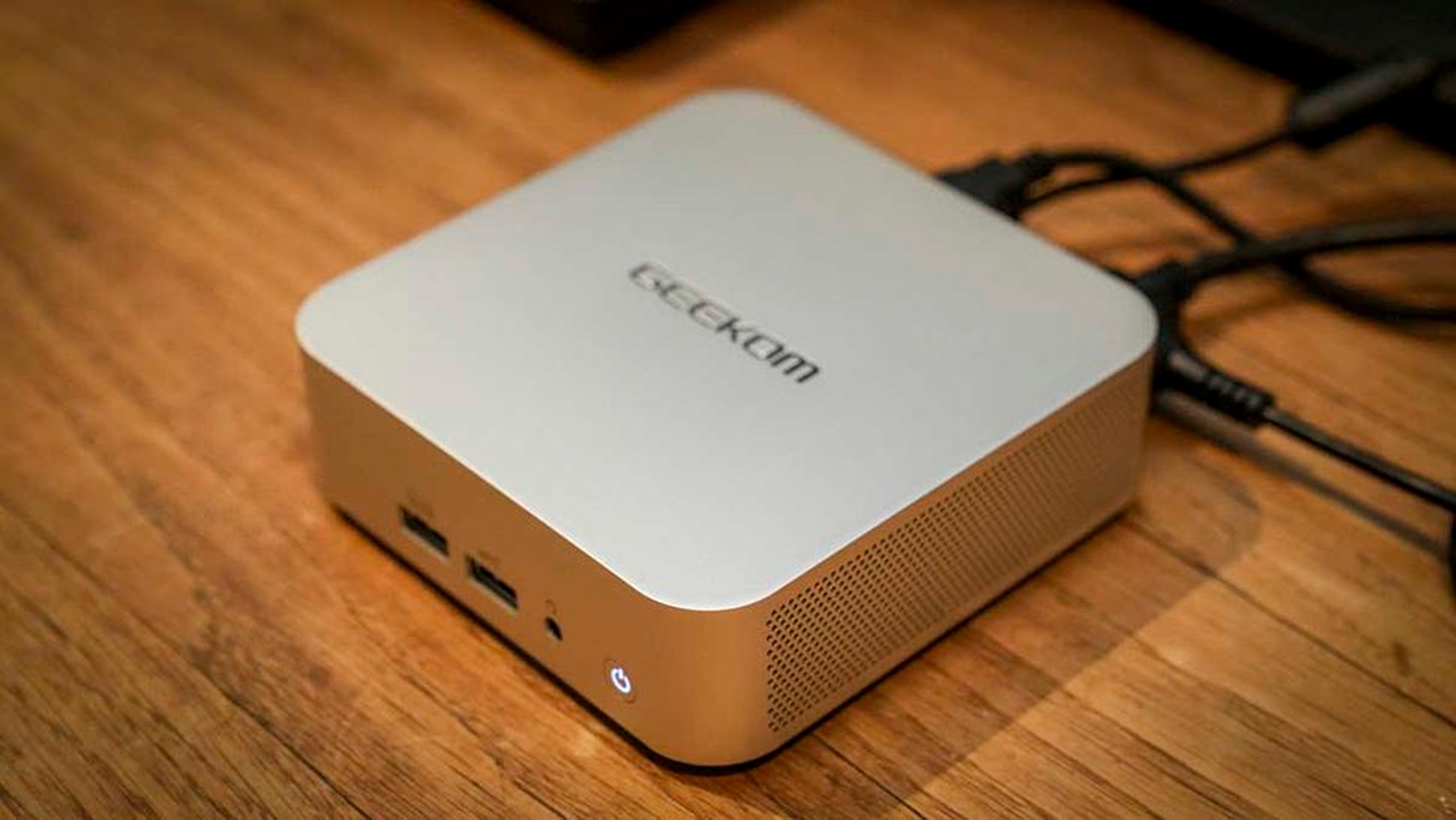 A sleek, metallic mini PC with the brand name on top, featuring USB ports and a power button. It's on a wooden surface, conveying simplicity.