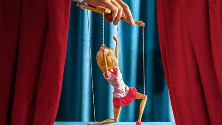 Hand controlling woman puppet on stage representing manipulation and humor.