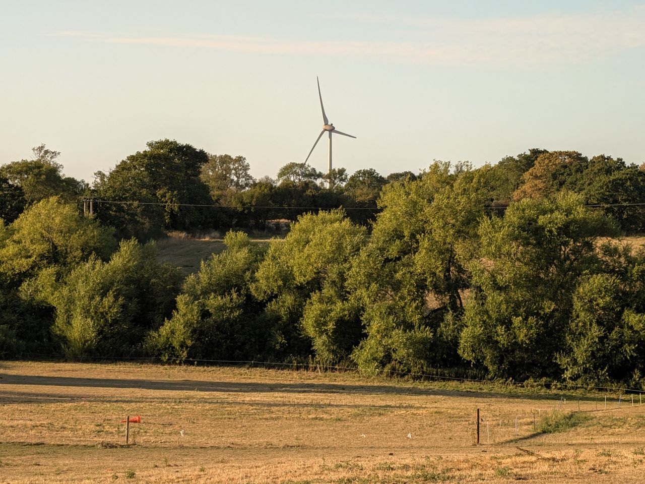 Wind turbine overlooking dry fields and trees in the countryside at sunset.
