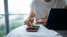 A woman uses the calculator app on her phone while sitting at a table in an office.