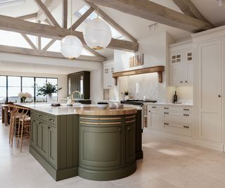 modern kitchen with shaker style units, green on island and cream for rest of ktichen, pale wooden ceiling beams and large white glass pendant lights above island