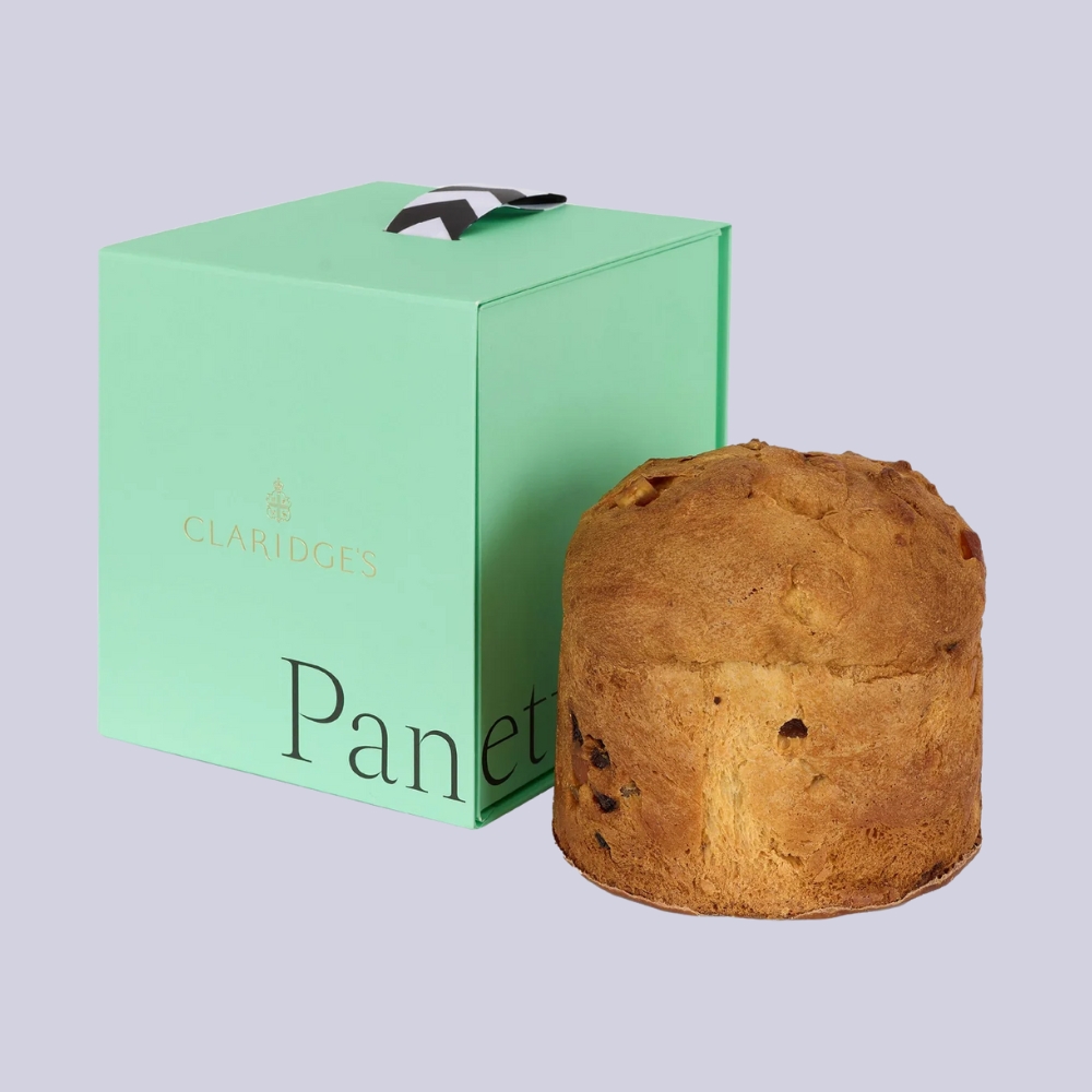 A sea green panettone box sits next to the festive cake against a pale lilac background.