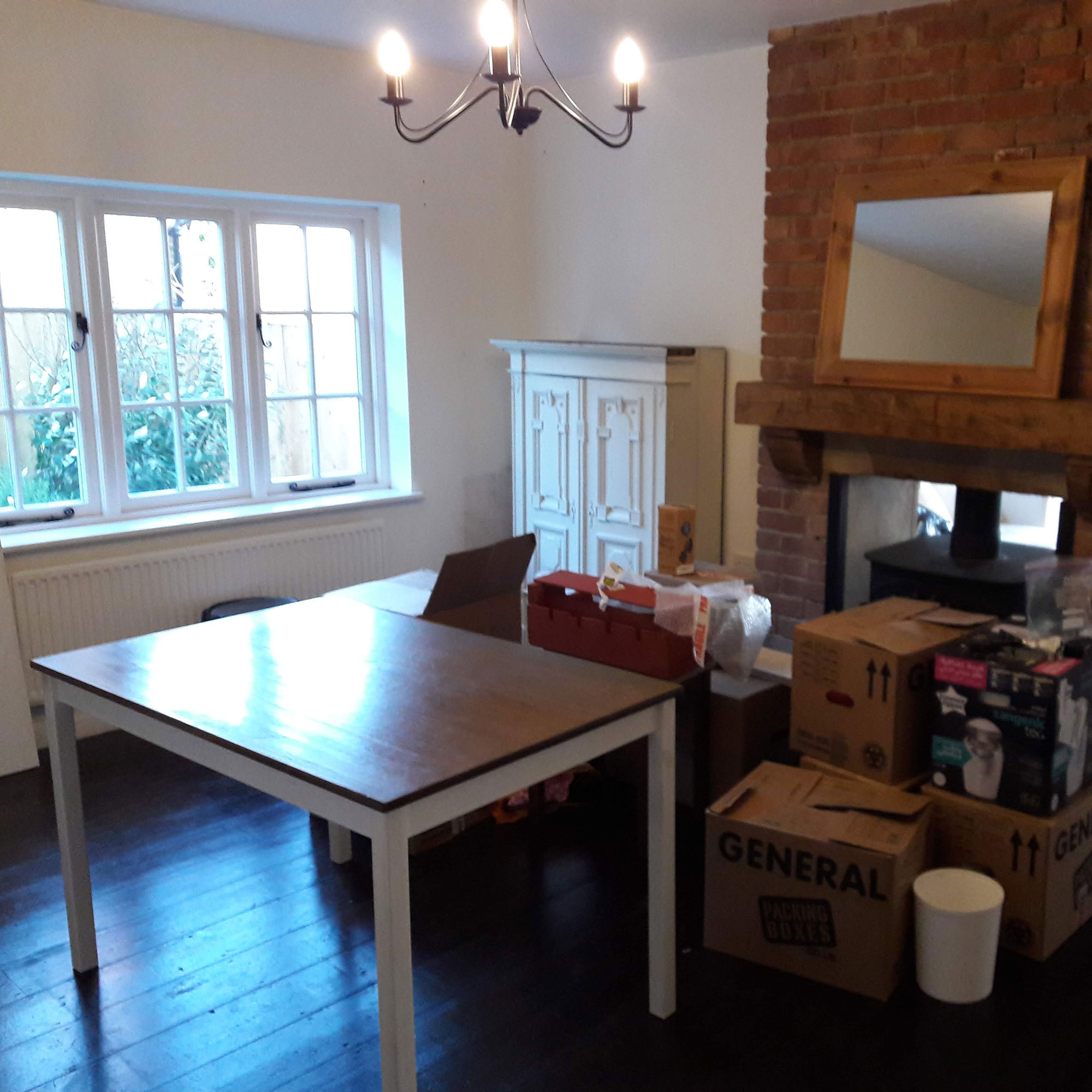 Room with wooden floor and square table surrounded by cardboard moving boxes to be unpacked