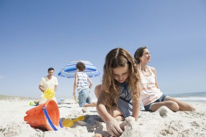 Little girl building a sandcastle with family in the background