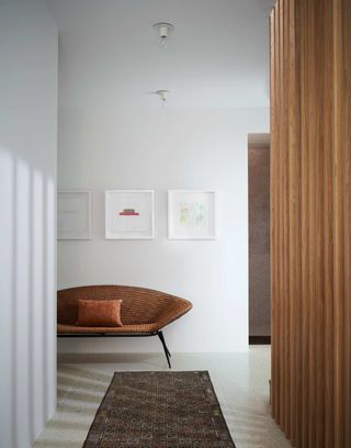 A rug in an entryway with a wooden partition and woven bench