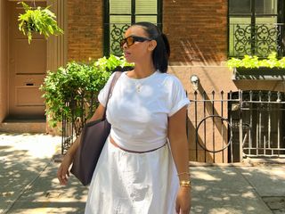 Aysha Sow wearing a white T-shirt and white skirt with a brown tote bag.