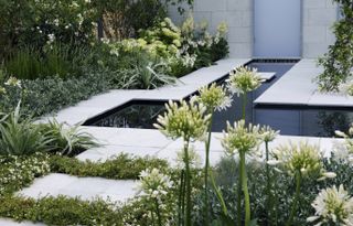 Geometric layout in a small garden with a water feature in the middle of a paved garden, with flowers around the borders