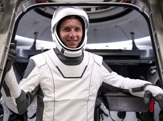astronaut standing in front of open spacecraft with a white spacesuit and helmet on