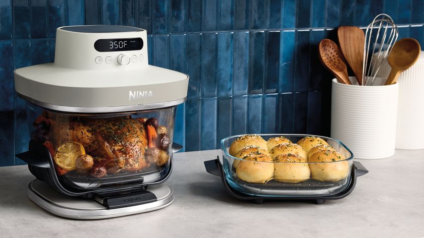 Ninja Crispi Pro air fryer containing roast chicken beside a dish of bread rolls on a kitchen counter