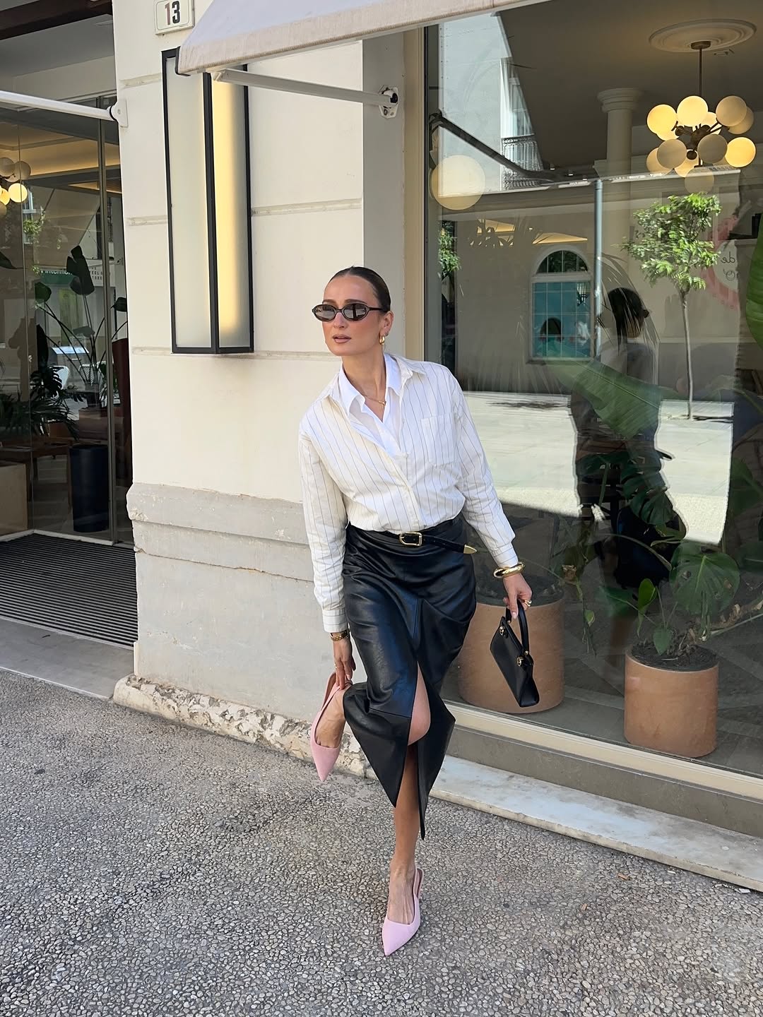 An image of woman wearing light pink shoes, one of the biggest 2026 shoe color trends, with white button-down shirt and black skirt.