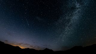a meteor streaks through a starry sky above a desert