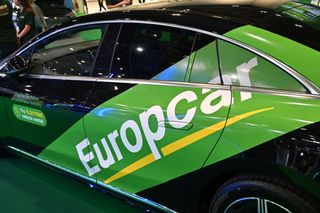 A black car on a showroom floor with a large banner painted on its side showing the words Europcar