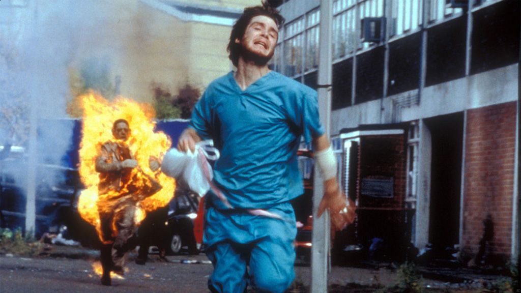 Jim runs away from a zombie on fire chasing after him in 28 Days Later.