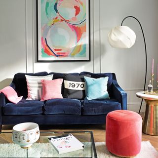 living room with wall art, navy velvet sofa pink velvet stool and scattered cushions arc lamp