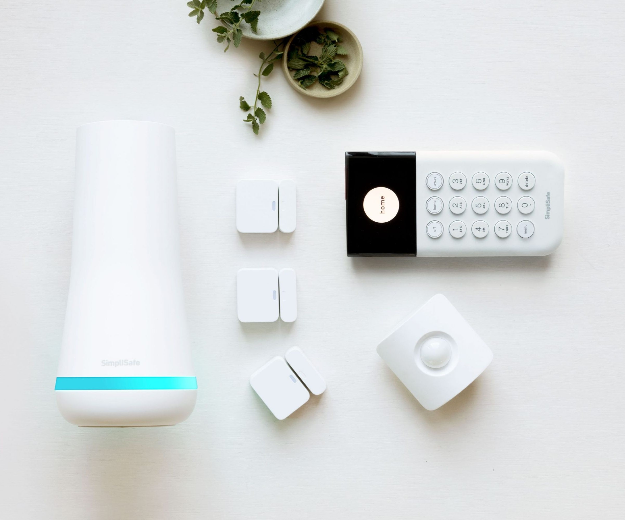 A white security device with a white and black controller and other white gadgets as seen from above with a small plant