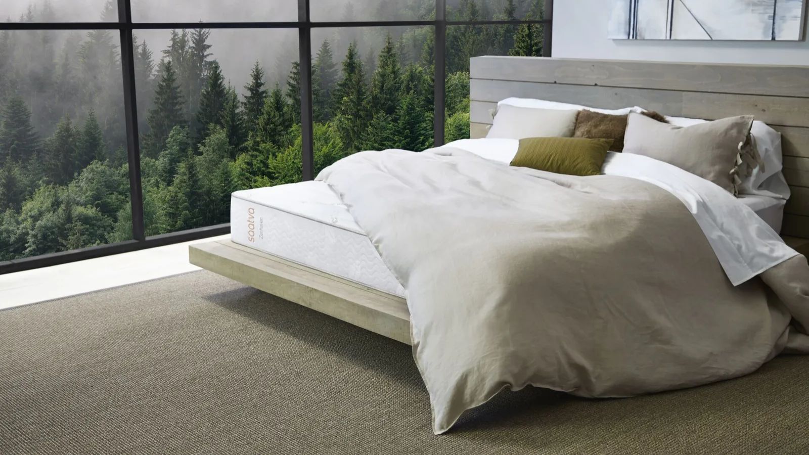 Saatva Zenhaven mattress in a bedroom with a wooden bed, rattan carpet, and large crittal windows to the left with a foggy landscape filled with trees