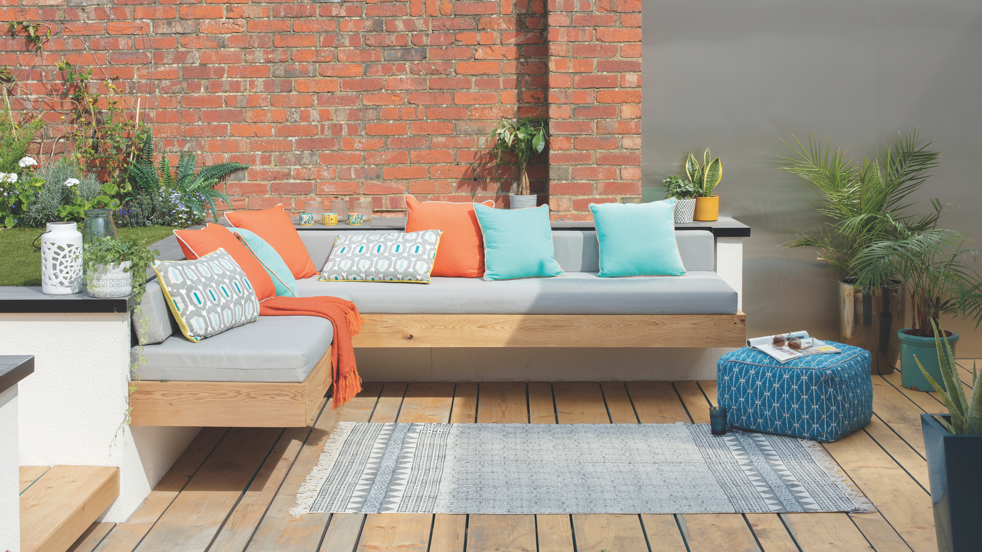 Gey/ blue outdoor rug on a wooden decking next to a built-in sofa.