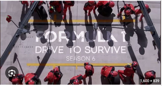 Overhead shot of pit crew in red overalls awaiting the arrival of F1 car in Formula 1: Drive to Survive season 6 on Netflix