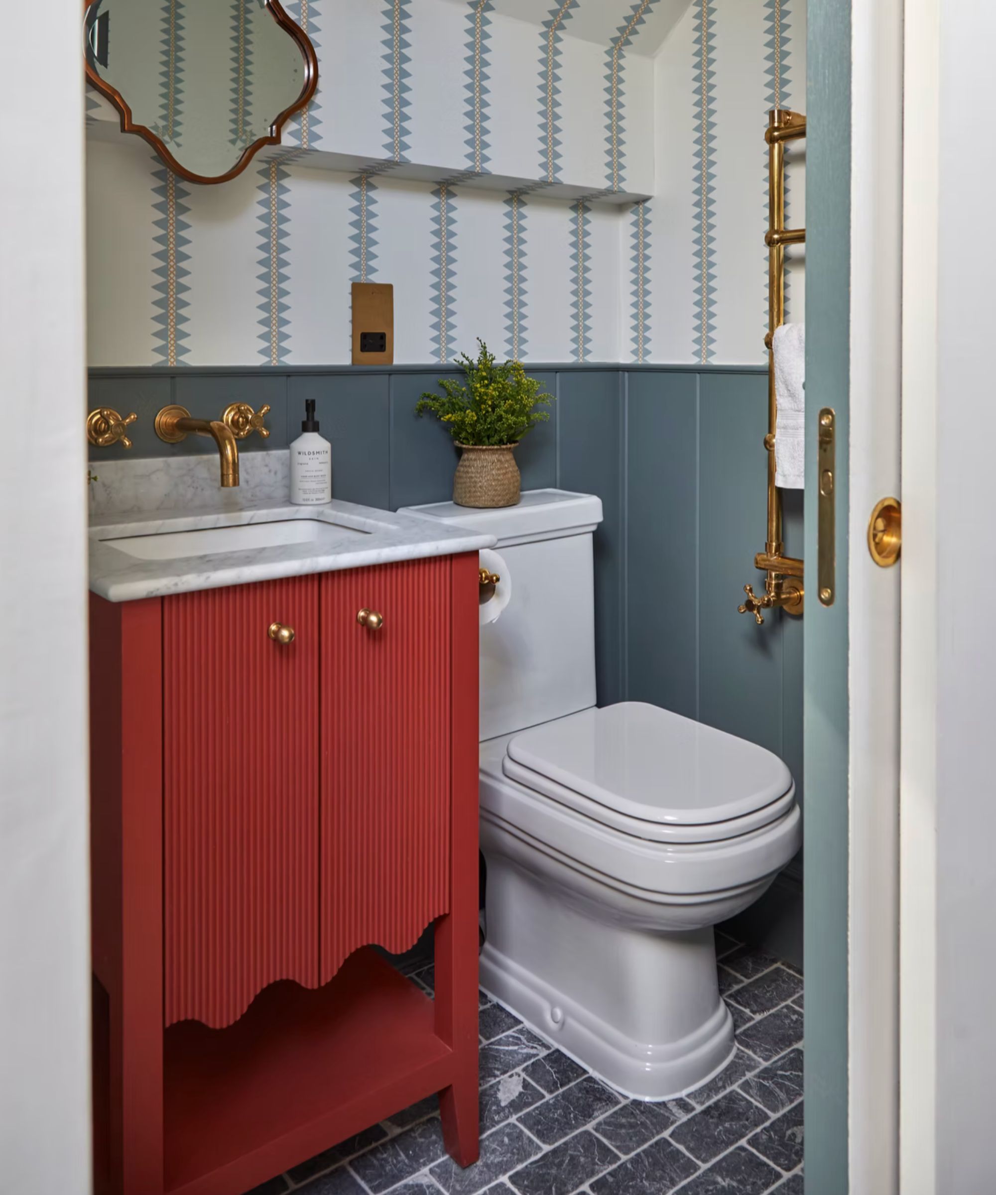 Bathroom with red painted vanity unit, blue painted panelling, tiled floor and striped wallpaper
