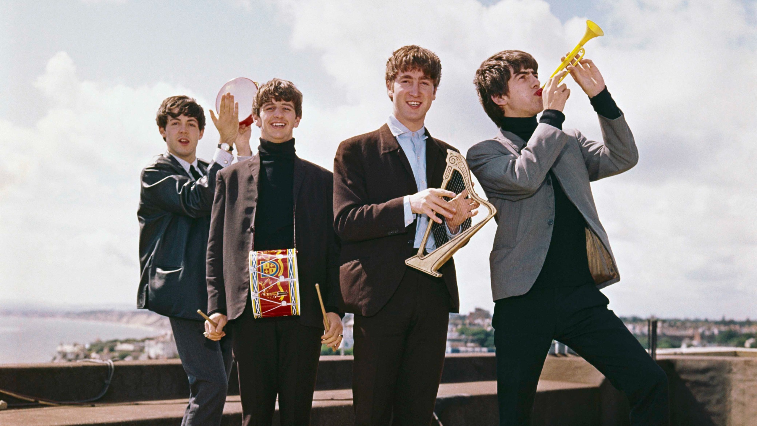 The Beatles band members on a rooftop playing instruments with blue sky behind them