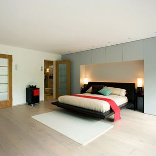 bedroom with white and grey wall bed with designed cushions wooden flooring and lamps