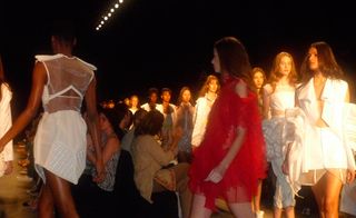 A model in a red outfit, walking in a line of models wearing white