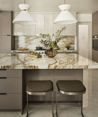 kitchen with gold toned veining, taupe units, bar stools, two white pendant lights, kitchen island,